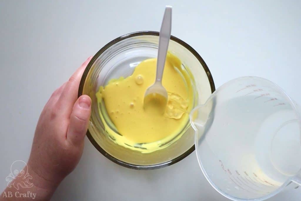 pouring a small amount of slime activator into a bowl with yellow glue