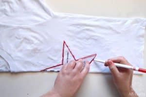 tracing around a star template with a washable marker on a folded white shirt