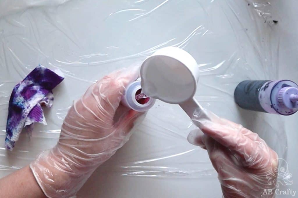 adding water with a measuring cup to a squeeze bottle that has some pink dye in it