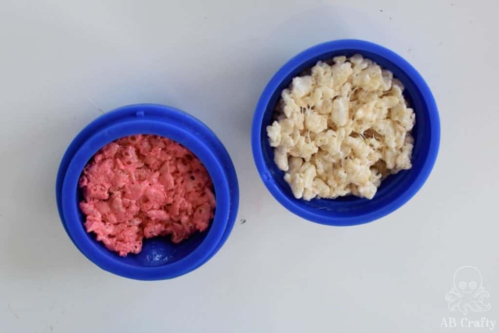 adding white and red rice krispie treat mixture to separate halves of a large sphere silicone mold