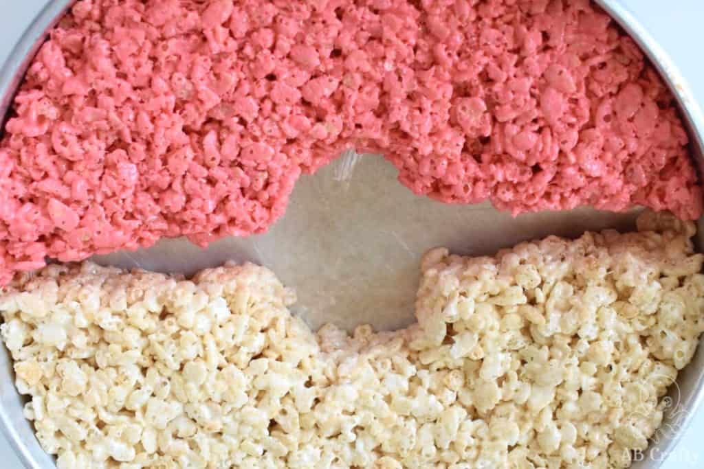 cake pan with half filled with red rice krispie treat and the other half with white, but with a center line and circle empty in the middle
