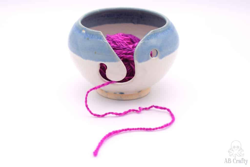 two toned ceramic yarn bowl with a blue stripe with pink yarn inside coming out of it