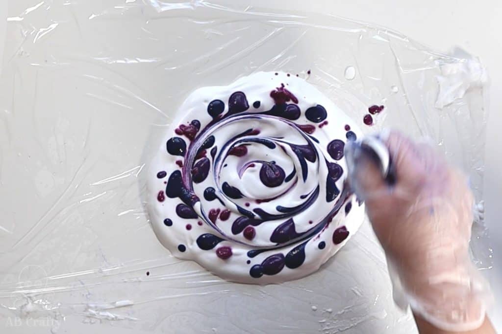 using a spoon to make a swirl within a circle of shaving cream and purple and pink dye on it