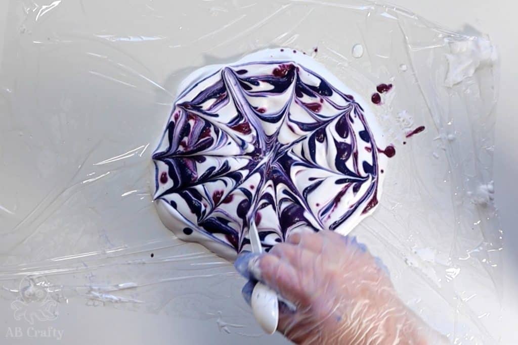 using a spoon to create lines across a circle of shaving cream with dye on it