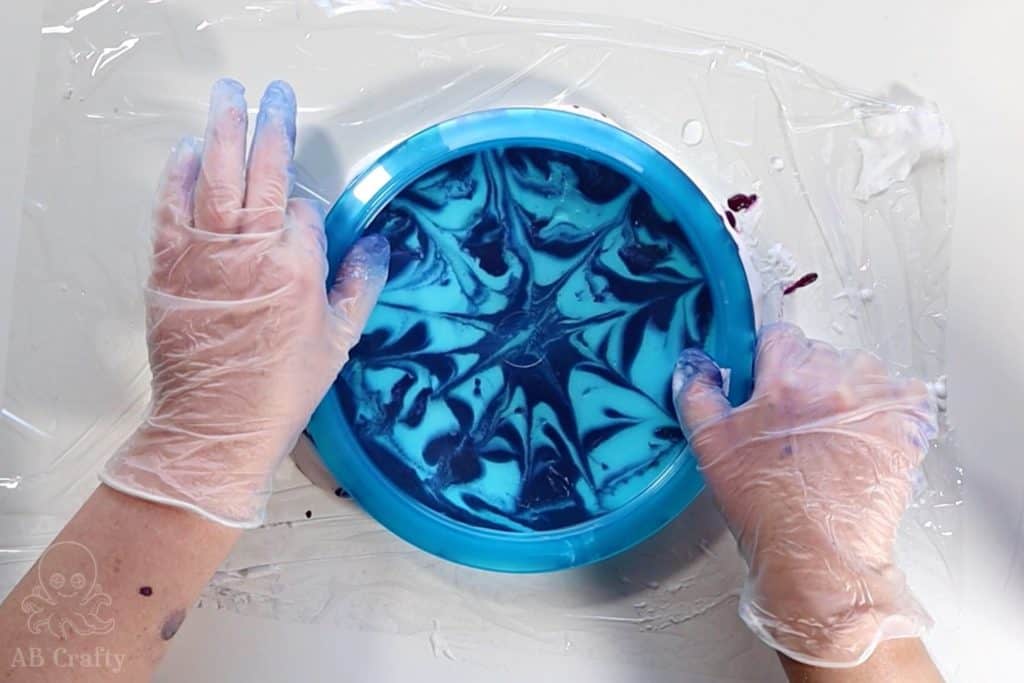 pressing a blue disc golf disc into shaving cream and dye on plastic wrap