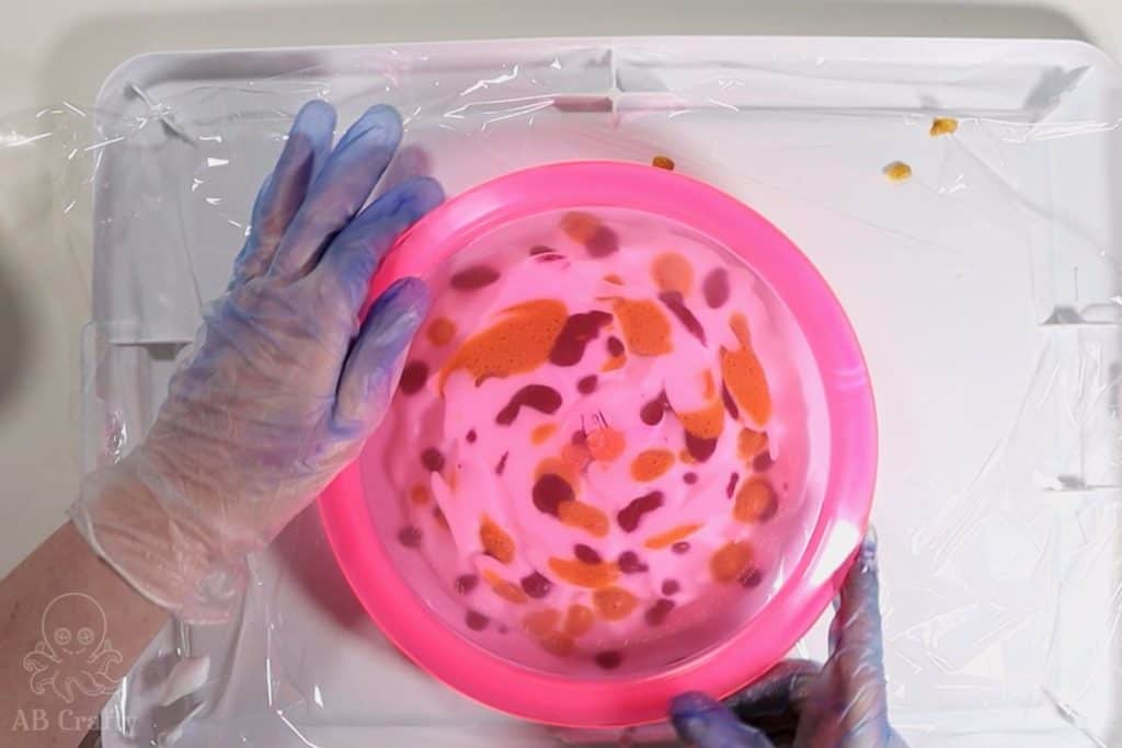 pressing a pink frisbee golf disc into shaving cream with pink and yellow dye