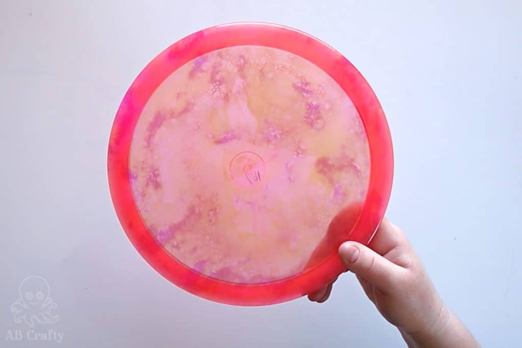 holding finished dyed pink disc golf disc with swirls of pink and yellow