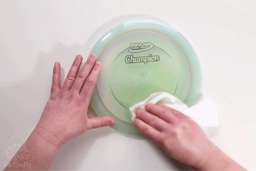 wiping a disc golf disc with a paper towel and acetone, removing the design