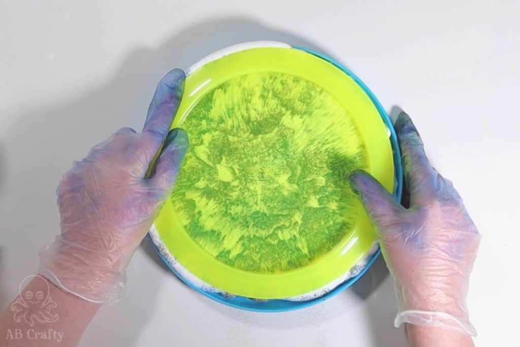 pushing a yellow disc golf disc into shaving cream and powdered dye in a plastic frisbee