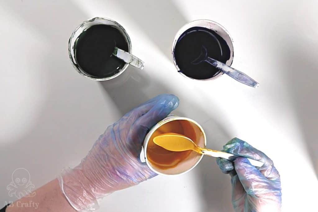 holding a spoon with mixed yellow synthetic dye in a cup