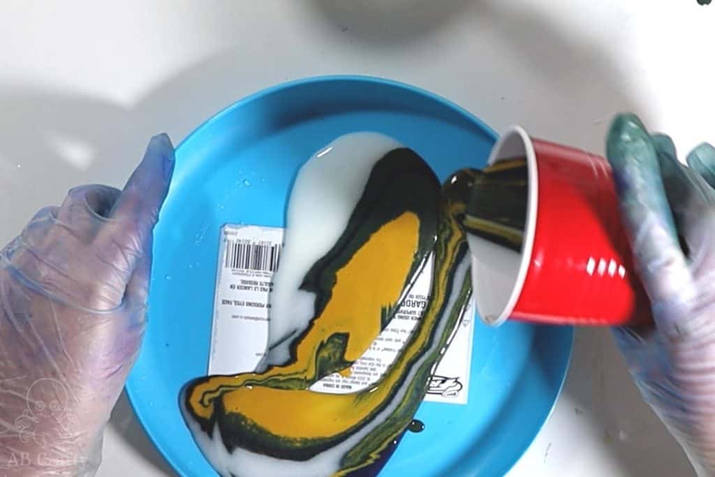 pouring dye and conditioner from a red cup into a blue plastic frisbee