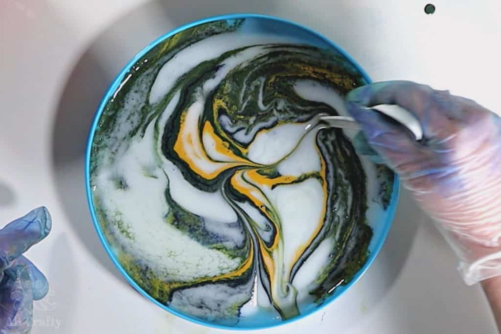 using a plastic spoon to swirl blue, yellow, and green dye and conditioner