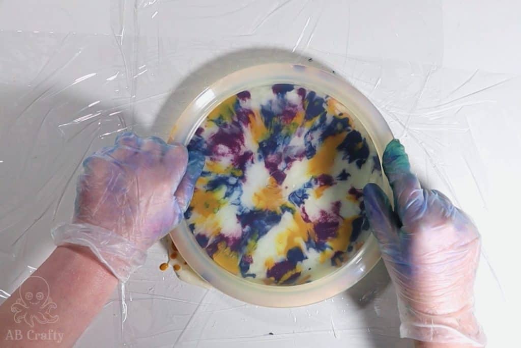 pushing a clear white frisbee golf disc into shampoo and synthetic dye on top of plastic wrap