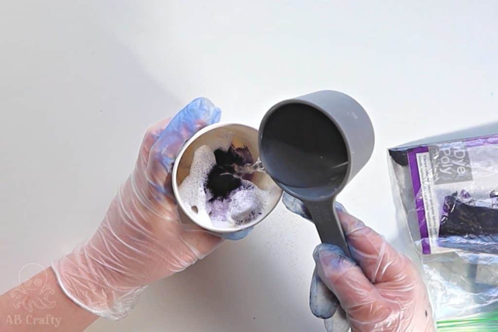 pouring water from a measuring cup into a paper cup with shaving cream and purple idye poly