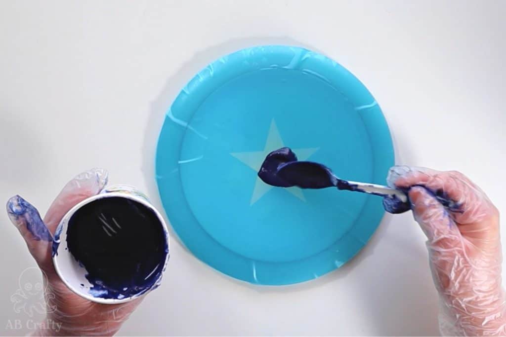 using a spoon to put dye into the open part of a star stencil on a disc golf disc