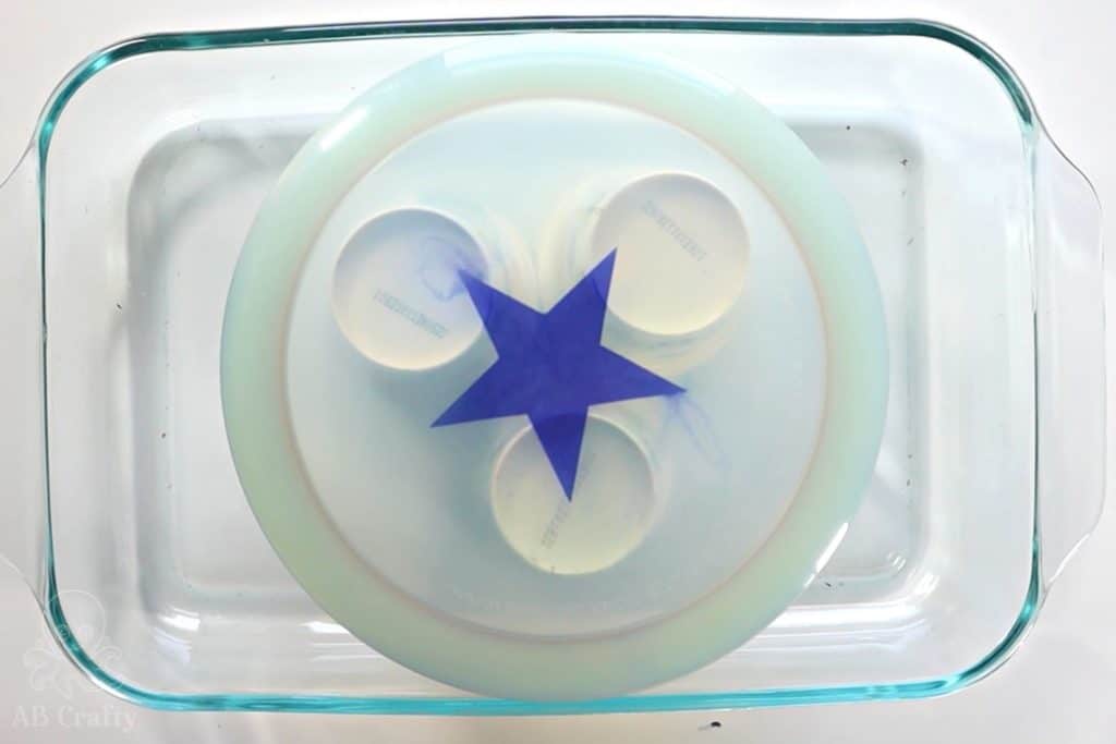 clear white disc golf with a dyed blue star in the middle, stacked on cups in a glass pan