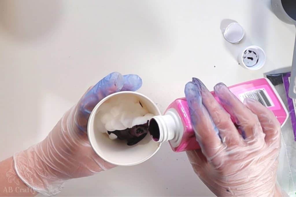 pouring pink synthetic dye from a bottle into a paper cup with shaving cream in it