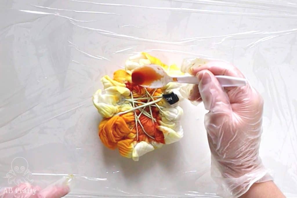 pouring orange dye from a spoon onto a tied up shirt with yellow and orange dye on it