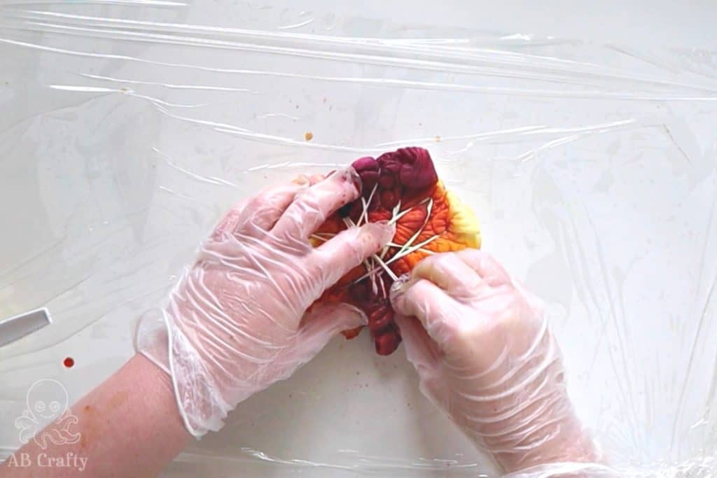 pressing red dye into a tied up shirt with yellow and orange dye on it