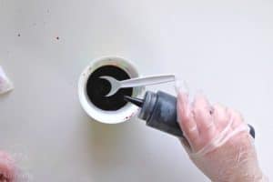 pouring dye from a squeeze bottle into a yogurt container with a plastic spoon in it