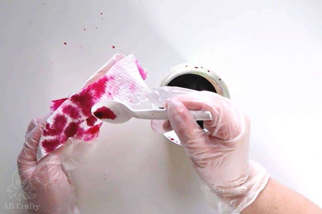 pouring dye from a plastic spoon onto a paper towel with different shades of pink on it