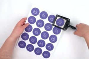 using a button punch to cut out the AB Crafty logo from a piece of paper with the logo printed across