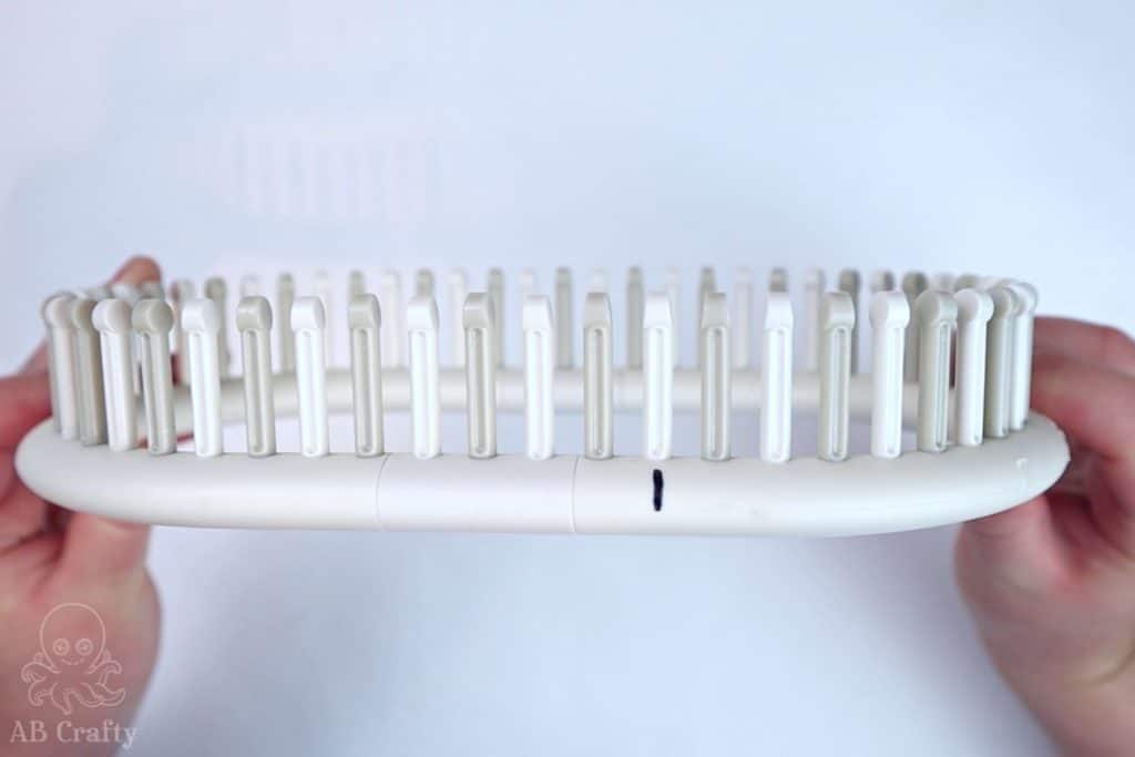 holding a white and grey adjustable knitting loom