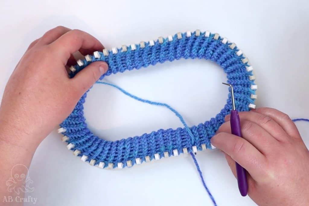 all of the first row of loops folded over and secured onto the pegs of the knitting loom