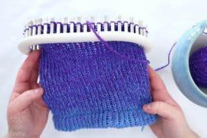 several rows of knitting on a knitting loom with a folded brim at the base, using blue to purple gradient hand spun yarn