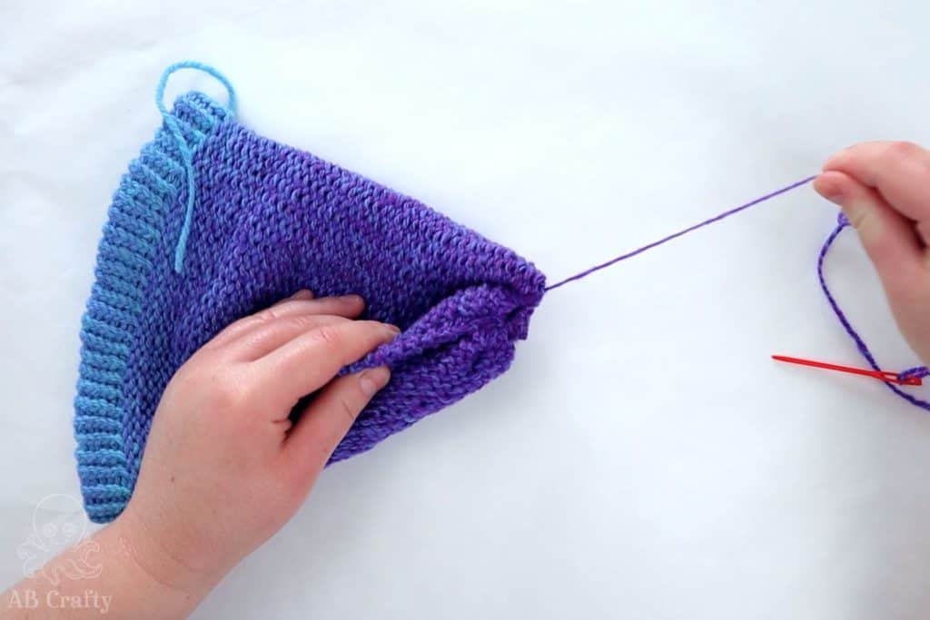 pulling the purple yarn to close the top of the loom knit hat