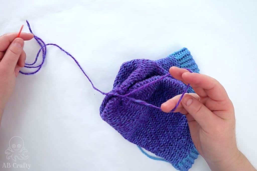 making a loop to create a knot at the top of the knit hat