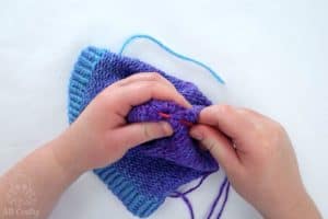 using a red plastic needle to sew through stitches at the top of the hat