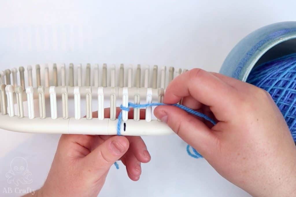 wrapping blue yarn around the first peg of an adjustable knitting loom