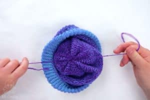 pulling the ends of the pom pom strings on the inside of the loom knitting hat to secure the knot