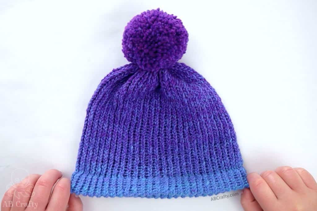 finished blue and purple loom knit hat with a double brim and purple pom pom