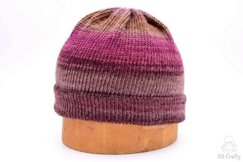 maroon, red, pink, and brown knit hat with a double brim on a hat block