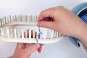 wrapping blue yarn on the second peg of a knitting loom