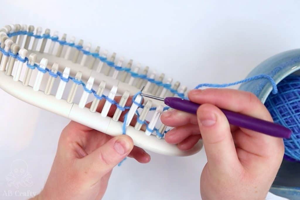 using a knitting loom hook to lift the bottom stitch