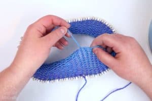 pulling the starting string of the knitting, showing the first 10 or so rows of the knitting loom