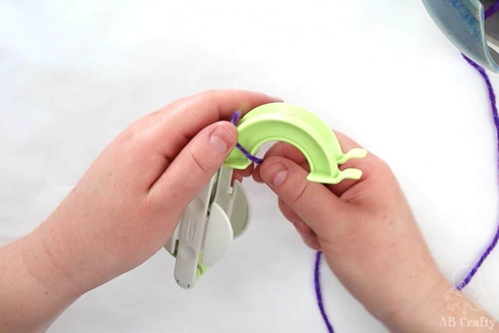 wrapping purple yarn around one side of a green clover pom pom maker