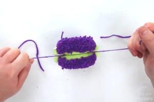 pulling a long strand of purple yarn to tighten