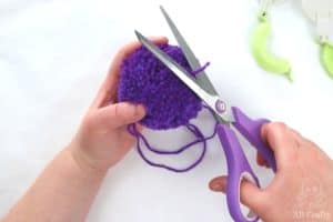 trimming the longer threads of the purple pom pom with scissors