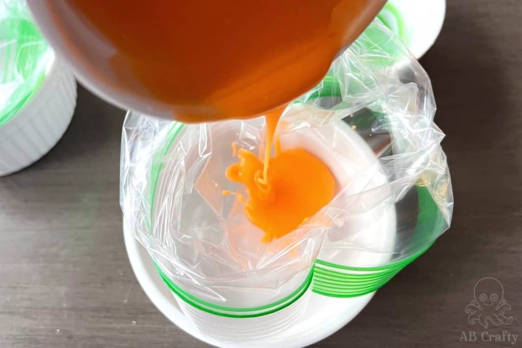 pouring orange icing into a plastic bag in a bowl