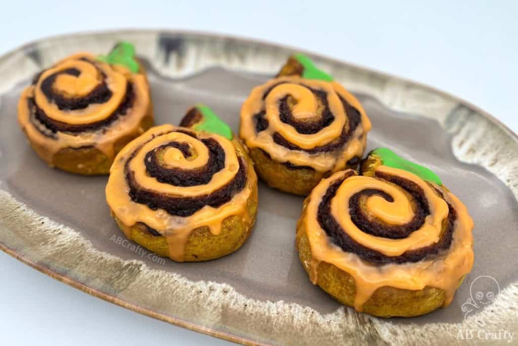 finished pumpkin cinnamon rolls with orange icing in a spiral and green icing for the stem