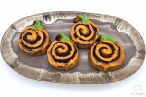 finished wildgrain pumpkin cinnamon rolls with orange icing in a spiral and green icing for the stem