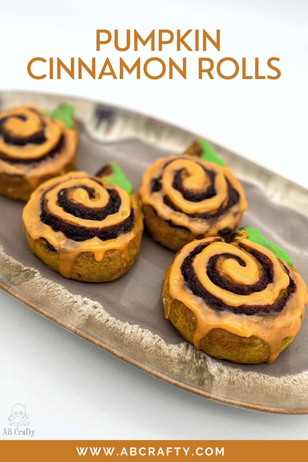 finished wildgrain cinnamon rolls with orange icing in a spiral and green icing for the stem and the title "pumpkin cinnamon rolls, abcrafty.com"