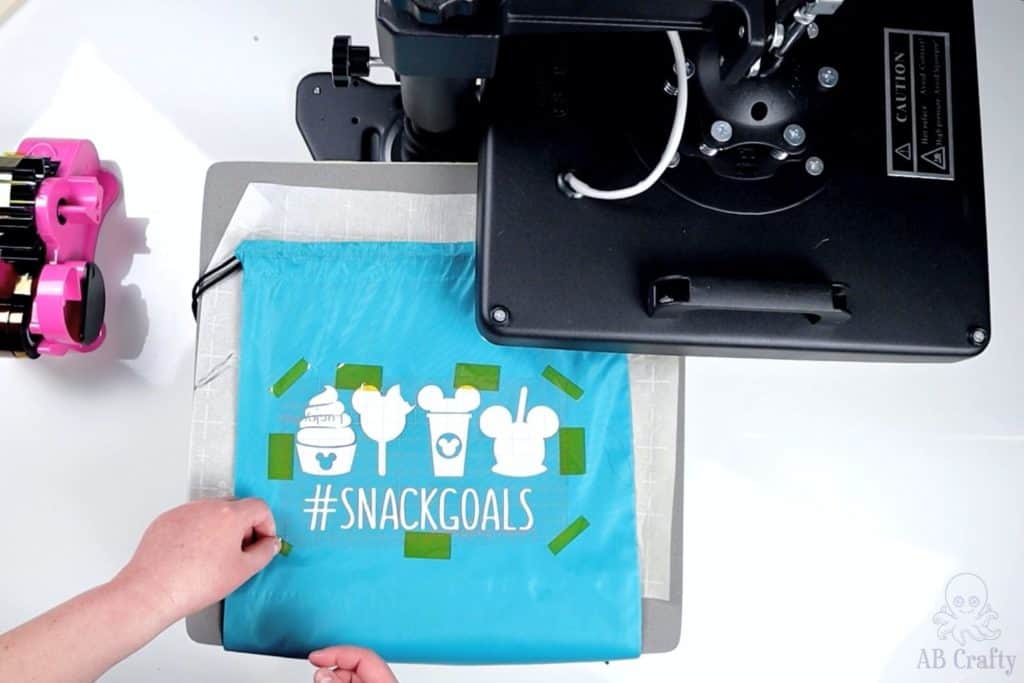 taping down a disney snacks design from sublimation paper onto a blue drawstring bag using heat tape