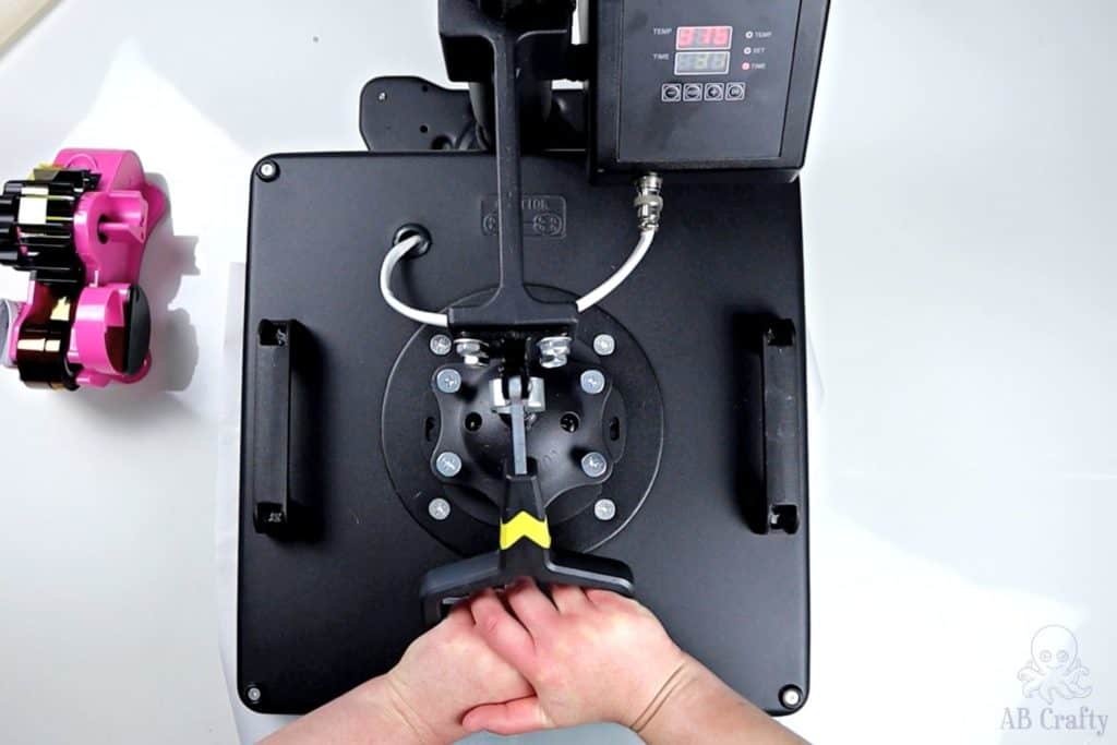 using both hands to pull down the lever on the heat press