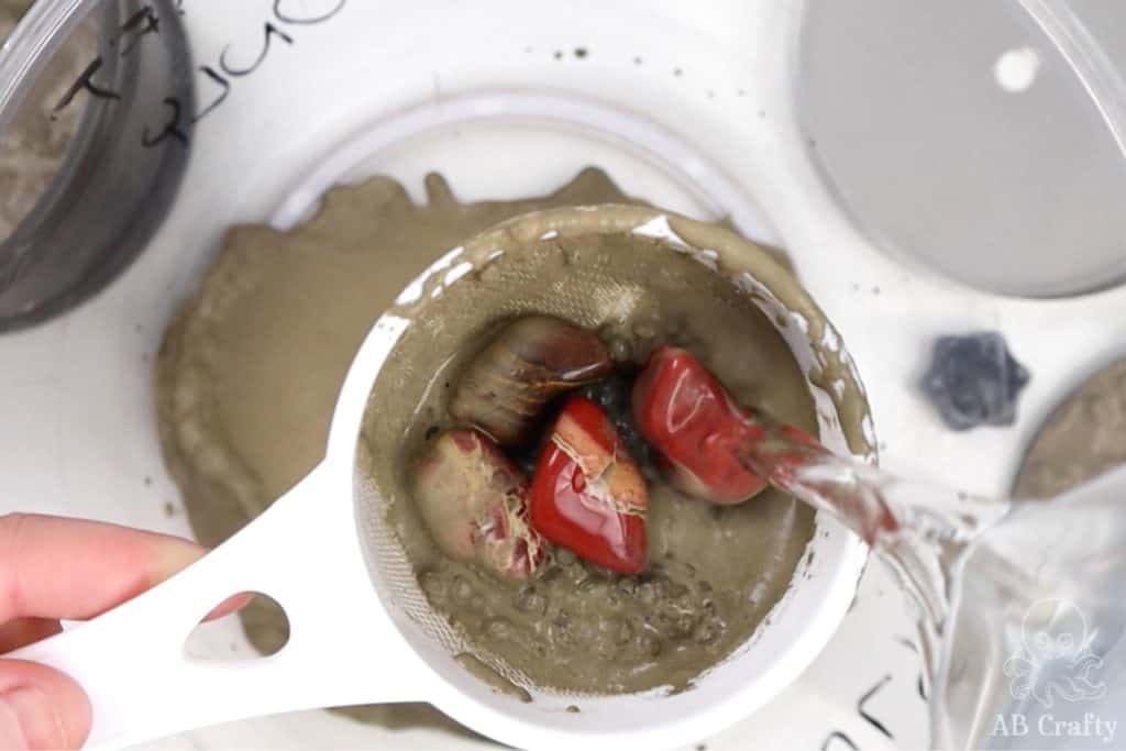 pouring water over jasper stones in a small sifter to clean the grit off