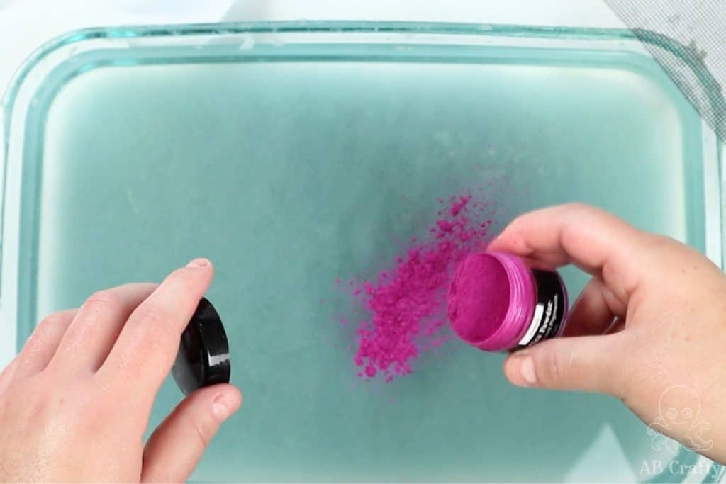 pouring pink mica powder into a dish of blue paper pulp and water